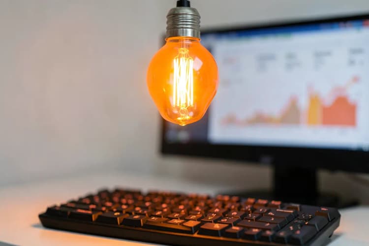 Lâmpada acesa sobre um teclado de computador com gráficos em uma tela desfocada ao fundo.